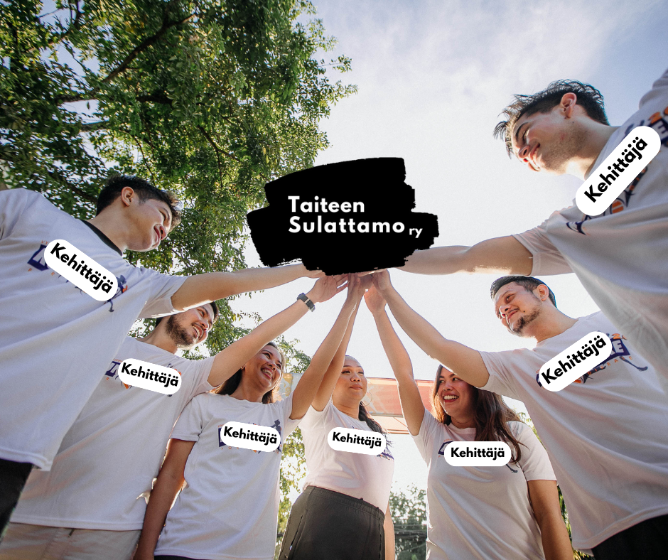 Seitsemän hymyilevää ihmistä seisoo puolikaaressa ja ovat vieneet  toisen kätensä yhteen kaaren keskelle. Valkoisissa t-paidoissa lukee rinnassa kehittäjä.